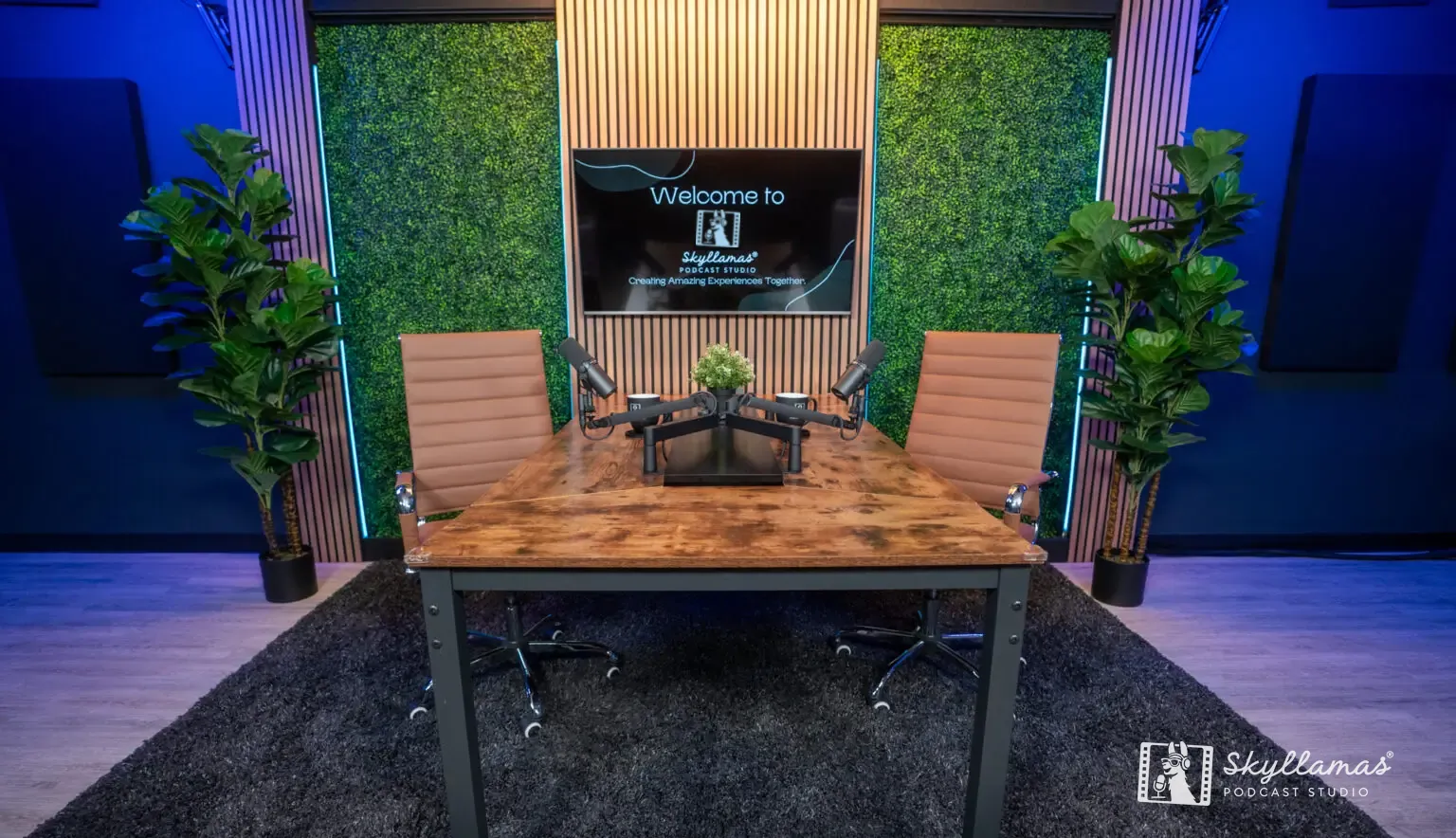 Podcast desk with microphones in front of a green wall and screen