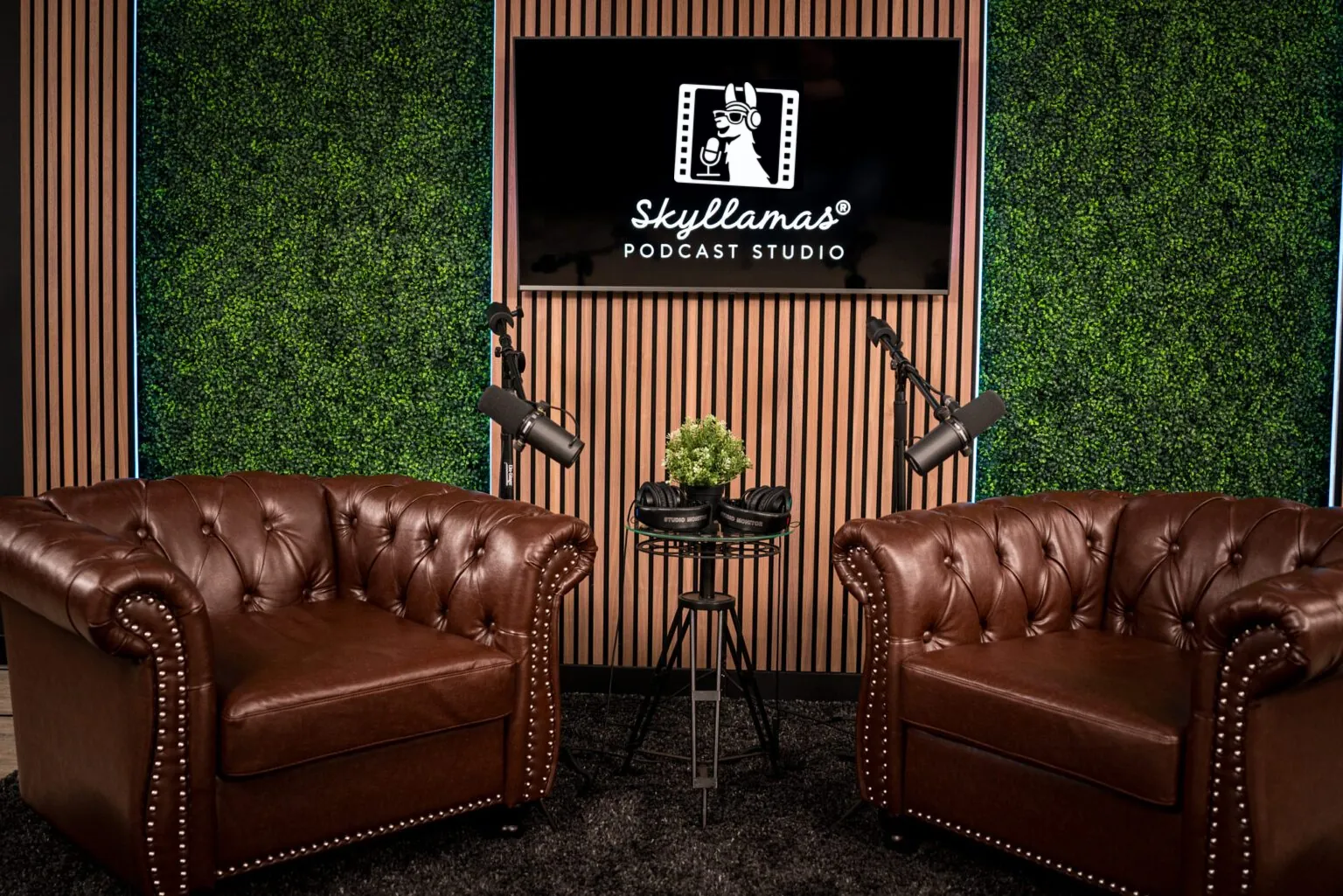 Leather armchairs facing each other on a podcast set with a green wall and studio cameras